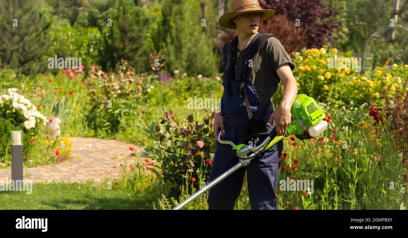 Un giovane uomo con un rasaerba si prende cura dell'erba nel cortile. Foto Stock