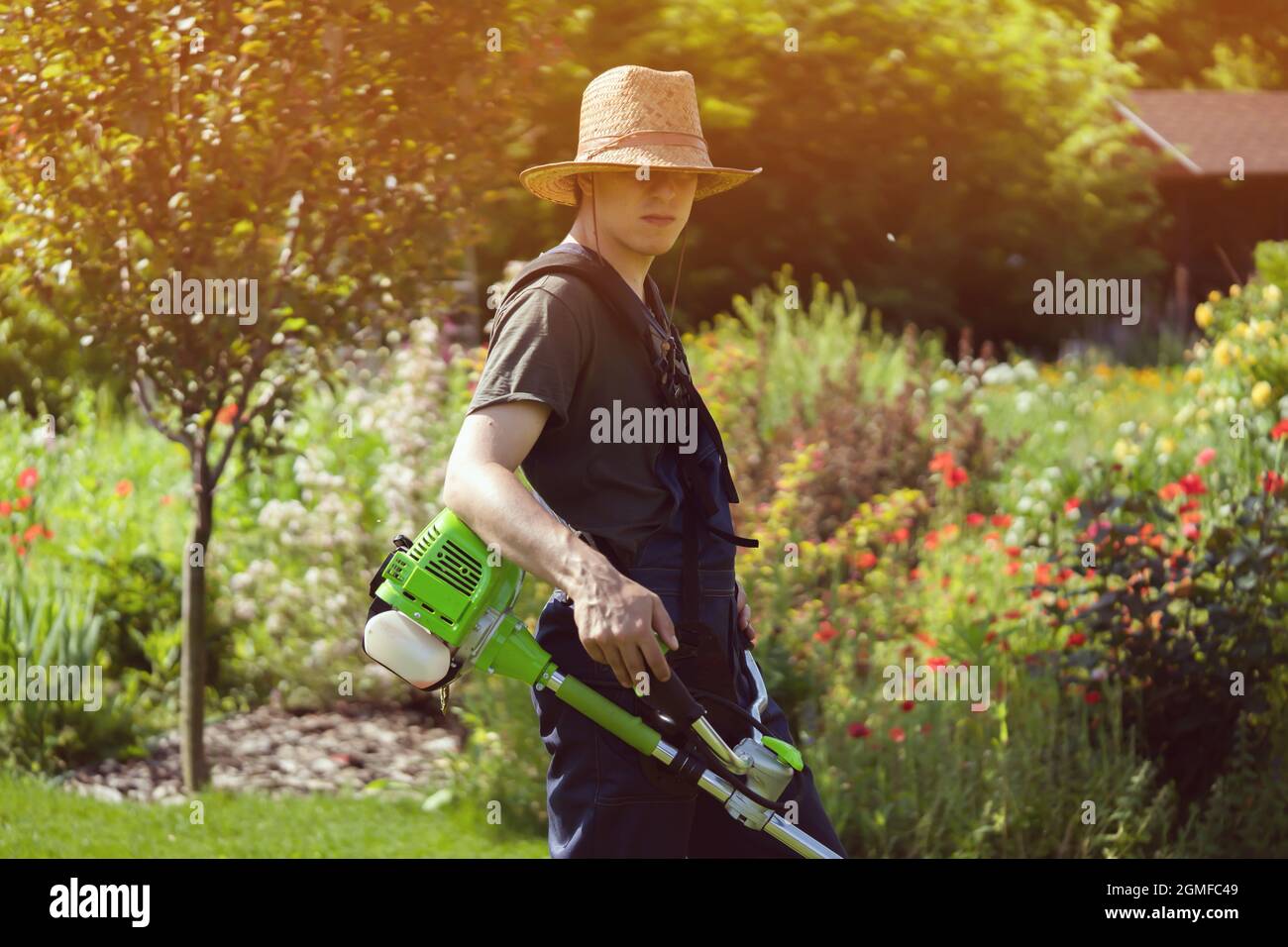 Un giovane uomo con un rasaerba si prende cura dell'erba nel cortile. Foto Stock