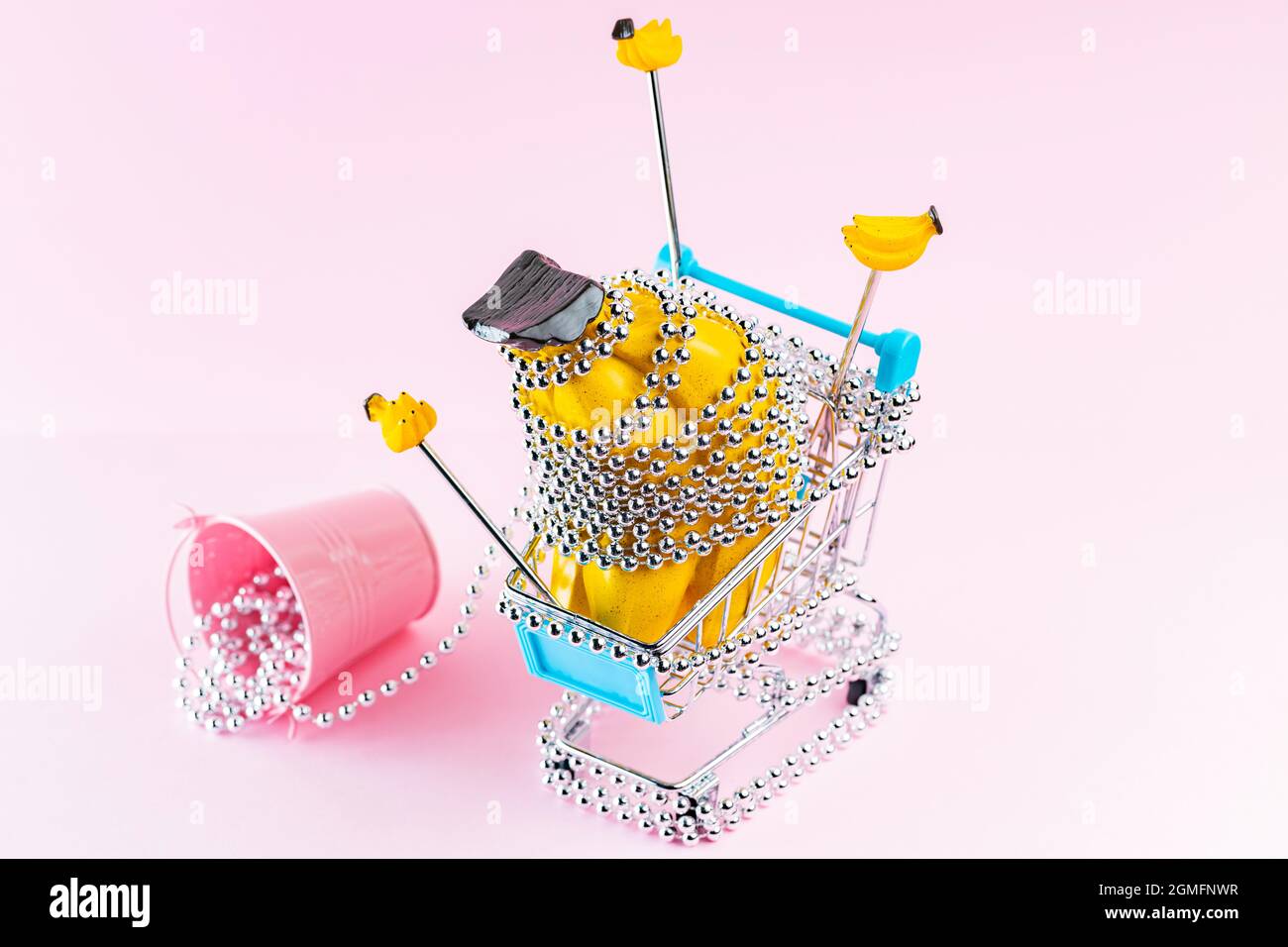 Carrello per lo shopping con perle di Natale in argento su sfondo rosa. Carrello con regali di Natale creativi. Decorazione di Natale concetto Foto Stock