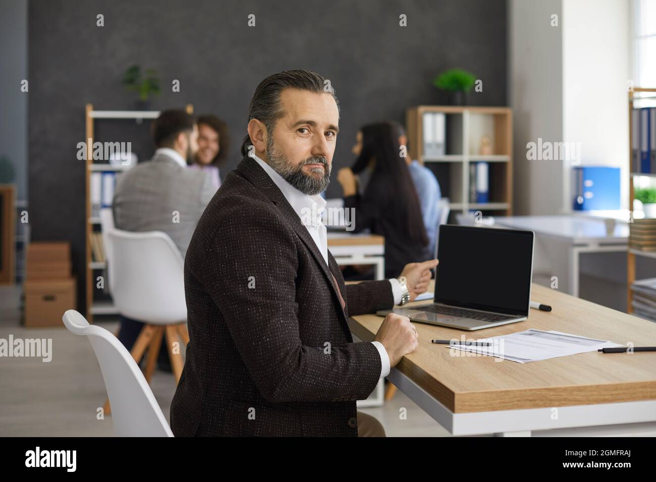 Ritratto del dirigente d'affari anziano seduto alla scrivania con il laptop nell'ufficio moderno Foto Stock