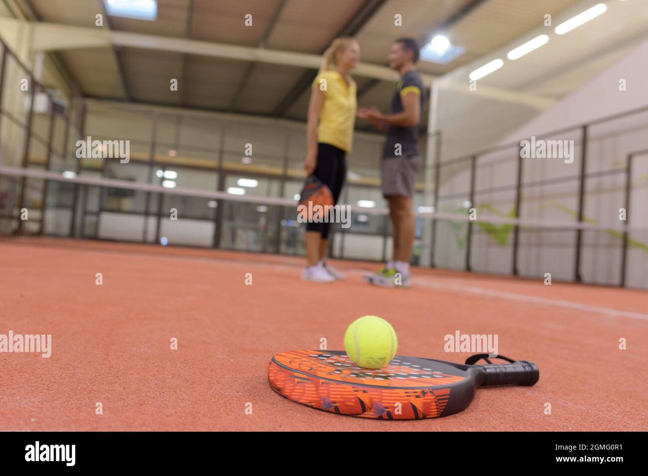 racket e palla da tennis in primo piano coppia parlare in background Foto Stock