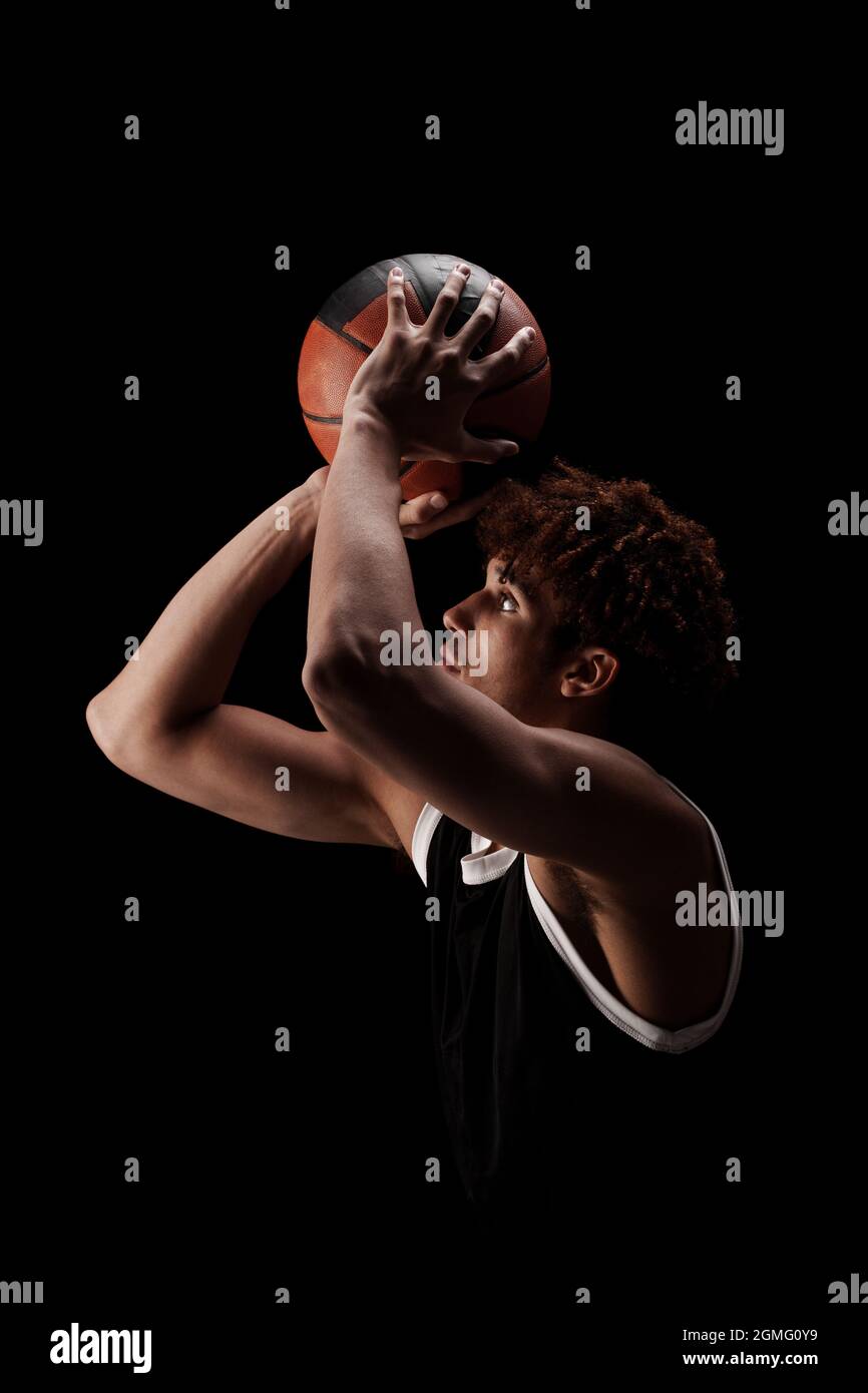 Giocatore di basket professionista che tiene una palla su sfondo nero. Serio concentrato afroamericano uomo in uniforme sportiva. Foto Stock
