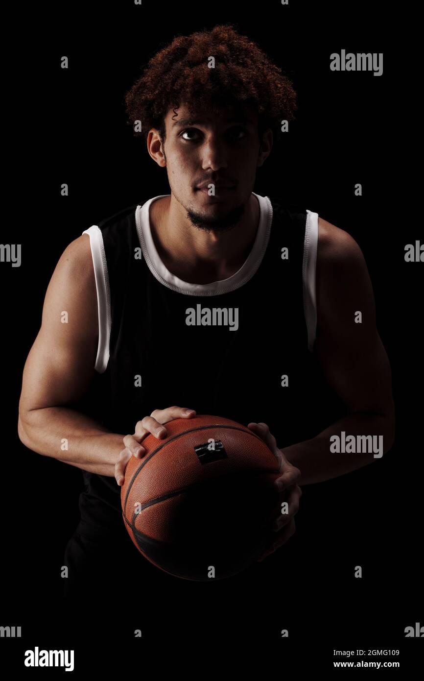 Giocatore di basket professionista che tiene una palla su sfondo nero. Serio concentrato afroamericano uomo in uniforme sportiva. Foto Stock