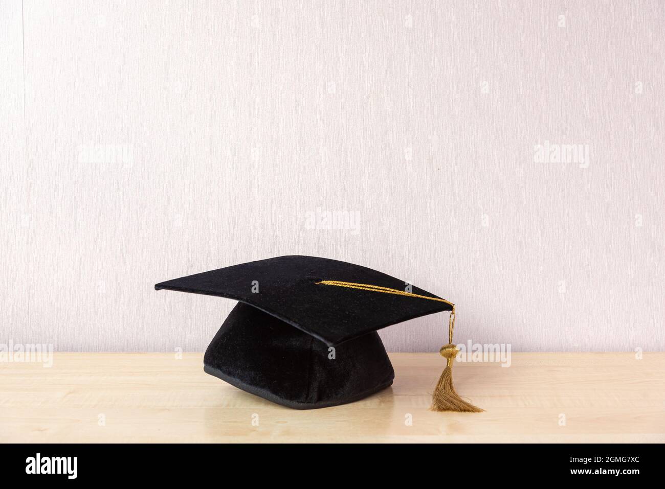 Cappellino accademico con nappina su tavolo in legno vicino a parete pastello Foto Stock