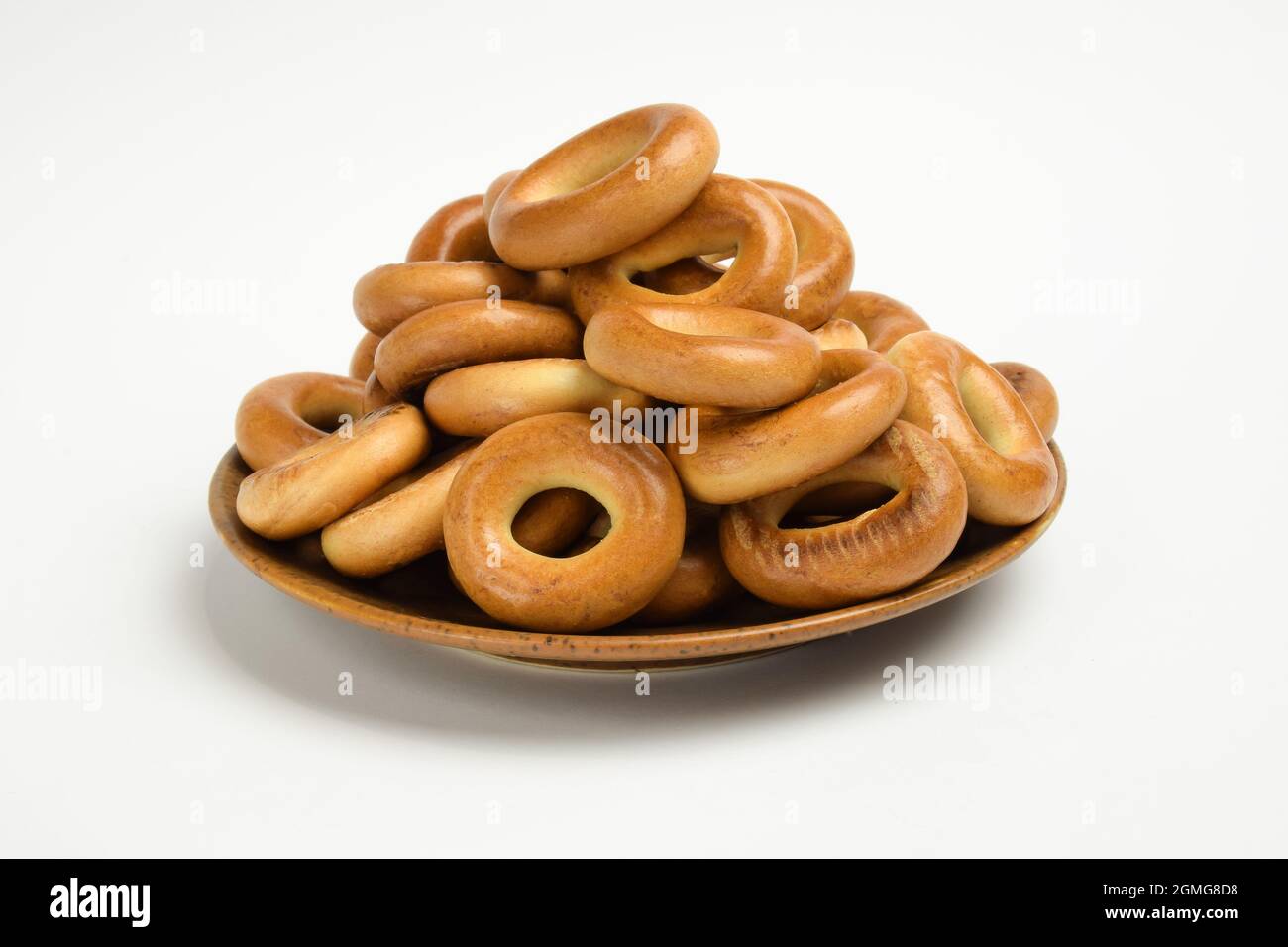 Su un piatto di ceramica marrone si trova un mucchio di bagel su uno sfondo bianco per la correzione Foto Stock