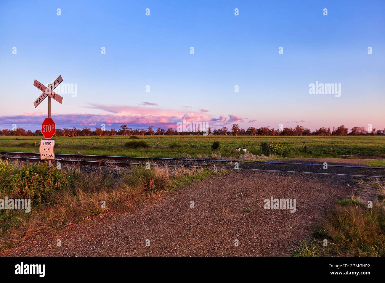 Attraversamento ferroviario di ghiaia non sigillato su campi agricoli vicino rurale australiano Moree città sul bacino artesiale - paesaggio del tramonto. Foto Stock