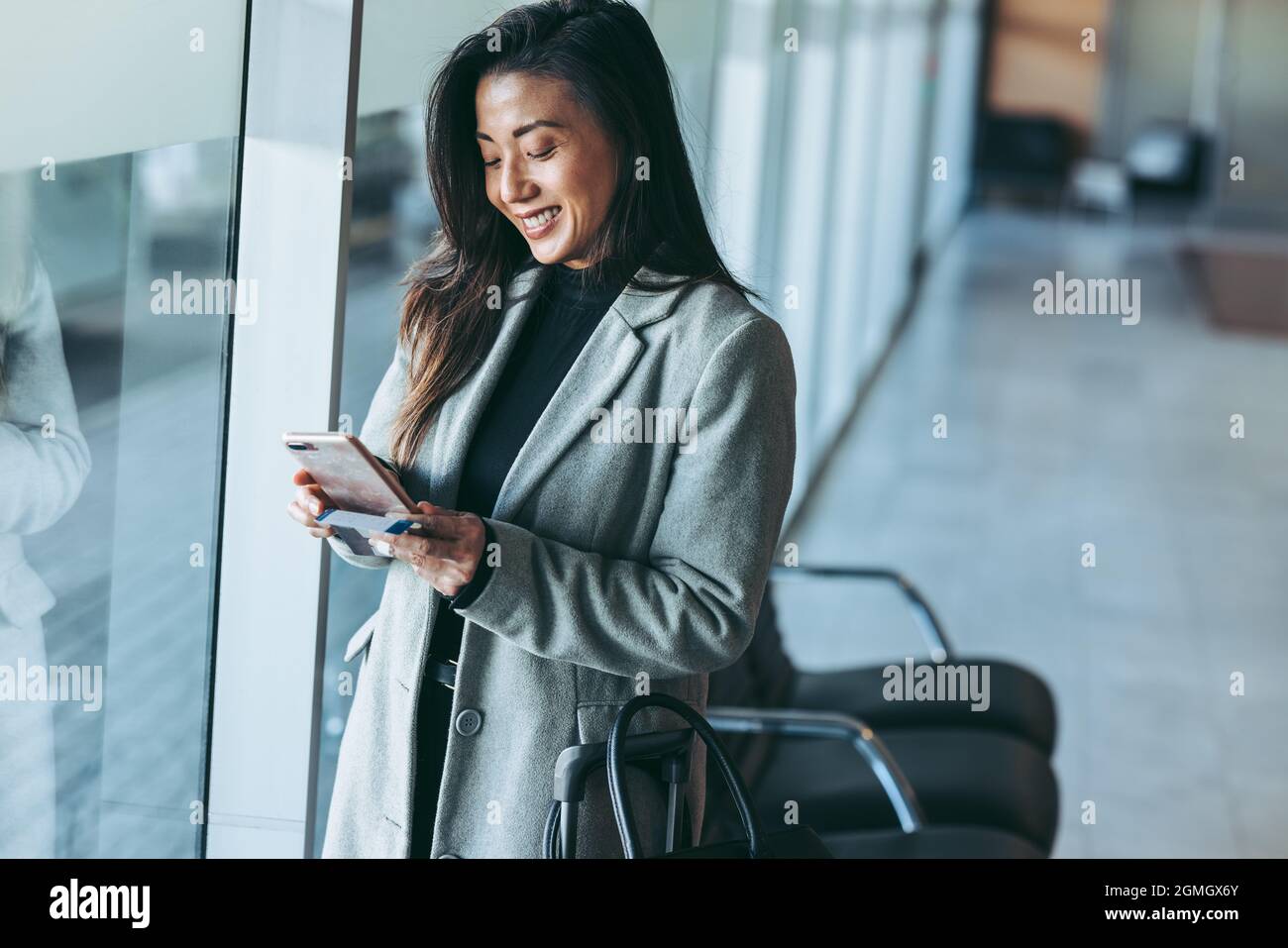 Donna in attesa presso la lounge dell'aeroporto utilizzando il suo telefono cellulare. Sorridente viaggiatore d'affari all'aeroporto in attesa del volo. Foto Stock