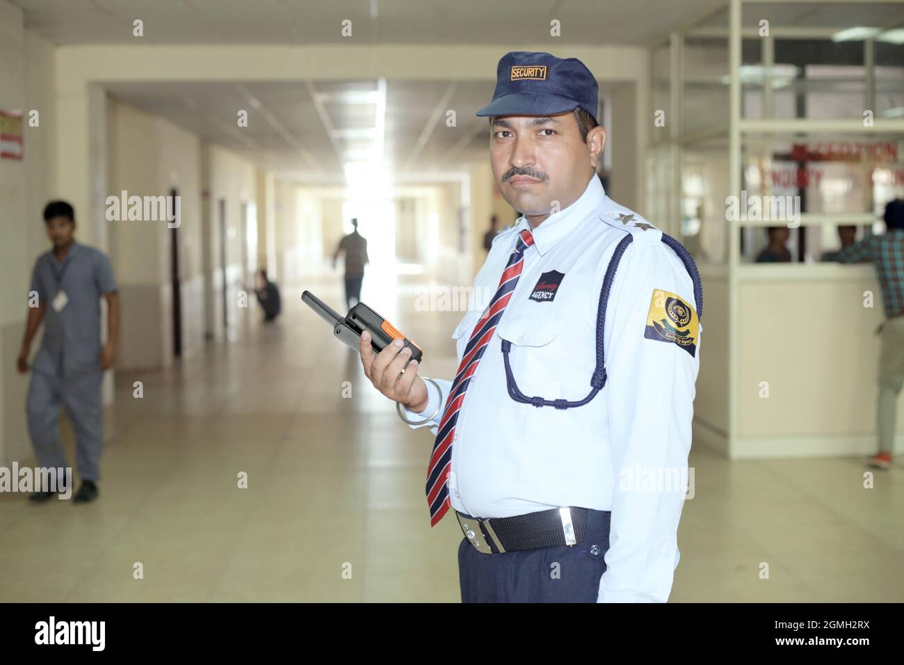 Addetto alla sicurezza in un ospedale in servizio con walkie talkie in mano in abito blu con cappuccio Foto Stock