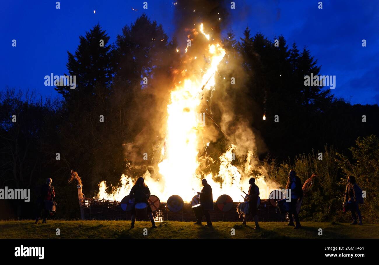 I membri dei batteristi del Pentacle si dilettano di fronte ad una barca vichinga cerimoniale in fiamme durante la barca equinox bruciano alla fattoria antica di Butser in Hampshire, per segnare l'equinox d'autunno e offrire Arrivederci ai lunghi giorni d'estate e accogliere la ricchezza del raccolto d'autunno. Data foto: Sabato 18 settembre 2021. Foto Stock