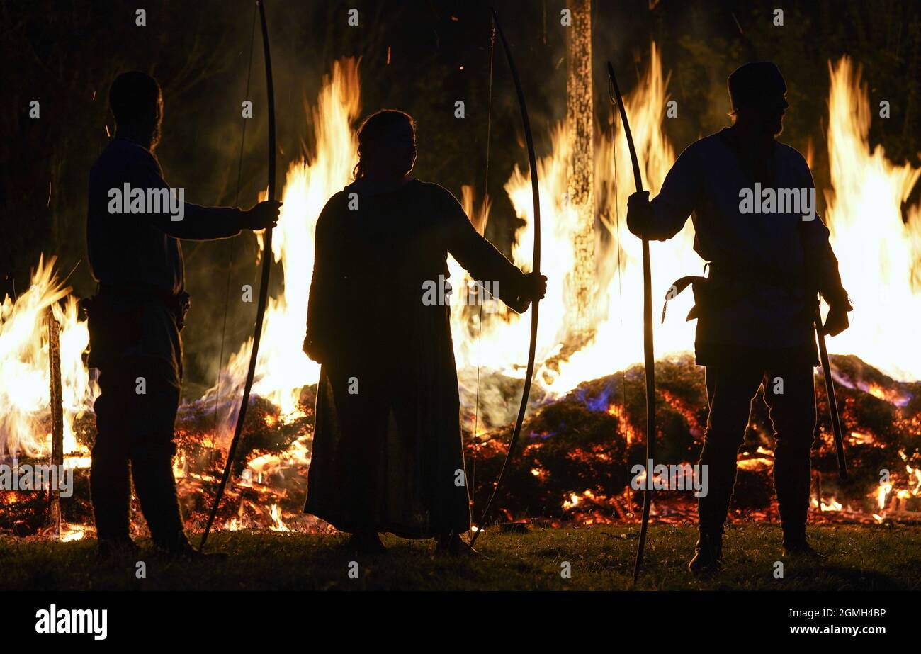 I membri del gruppo di storia vivente di Herigeas Hundas Saxons posano di fronte ad una barca vichinga cerimoniale in fiamme durante la combustione della barca Equinox alla Butser Ancient Farm in Hampshire, Per segnare l'Equinox d'autunno e offrire Arrivederci ai lunghi giorni d'estate e accogliere la ricchezza del raccolto d'autunno. Data foto: Sabato 18 settembre 2021. Foto Stock