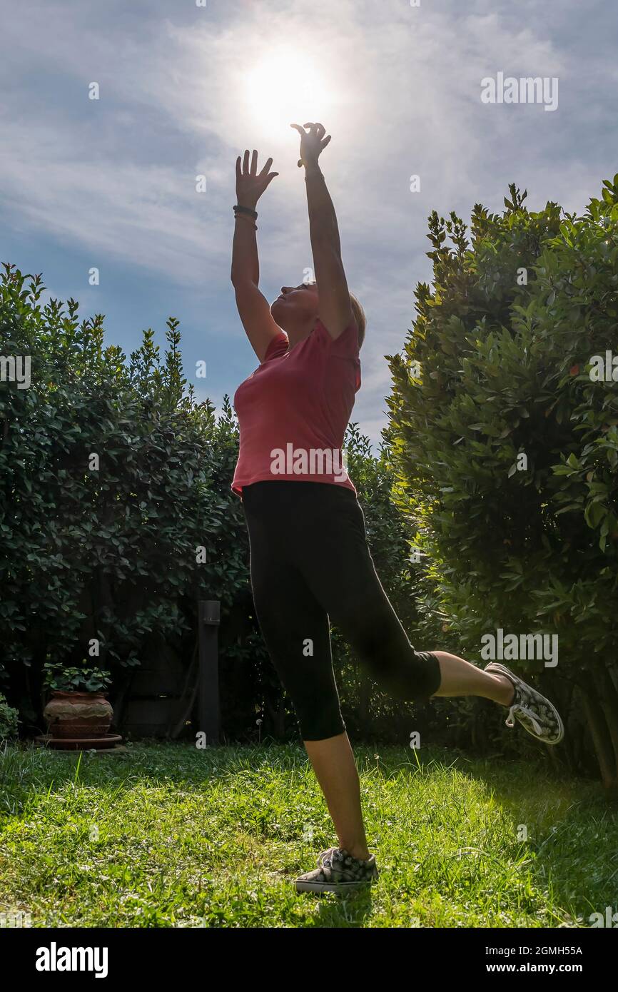 Una donna bianca di mezza età pretende di prendere il sole mentre si bilancia su una gamba Foto Stock