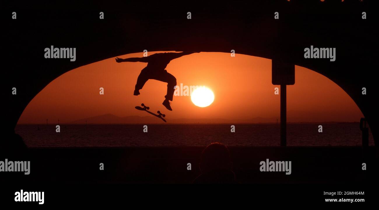 Silhouette al tramonto. Un pilota di skateboard esegue un trucco al tramonto a St Kilda, Melbourne , Australia . Foto Stock