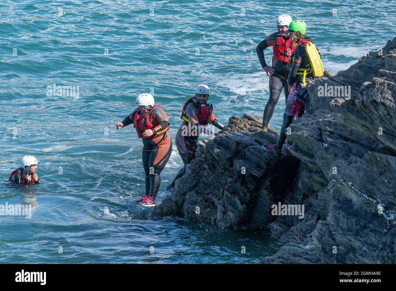 I vacanzieri saltano dalle rocce costellando con una guida su Towan Head a Newquay in Cornovaglia. Foto Stock