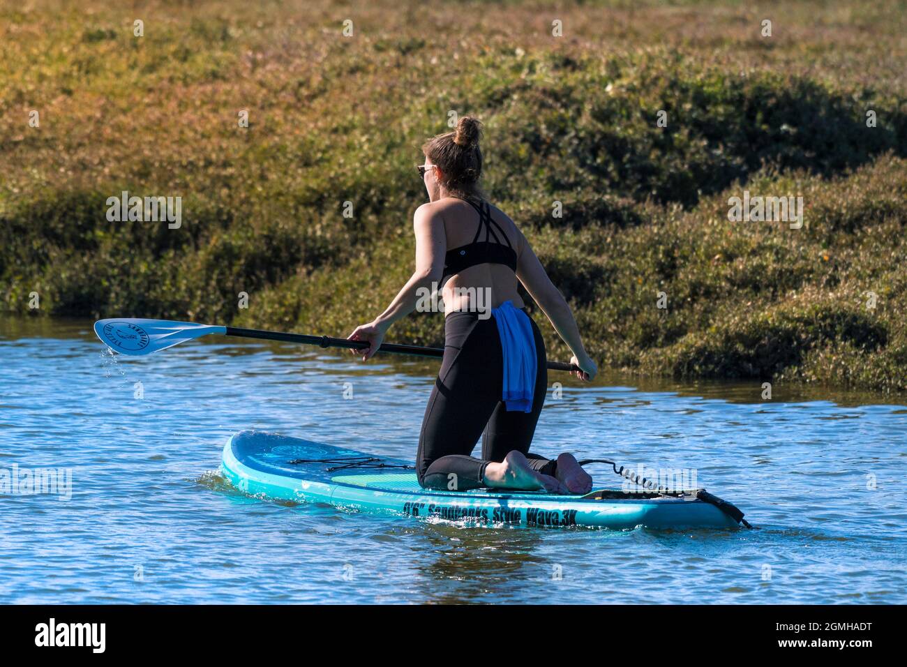 Una donna in vacanza inginocchiata su una tavola Stand Up in stile Sandbanks sul fiume Gannel a Newquay in Cornovaglia. Foto Stock