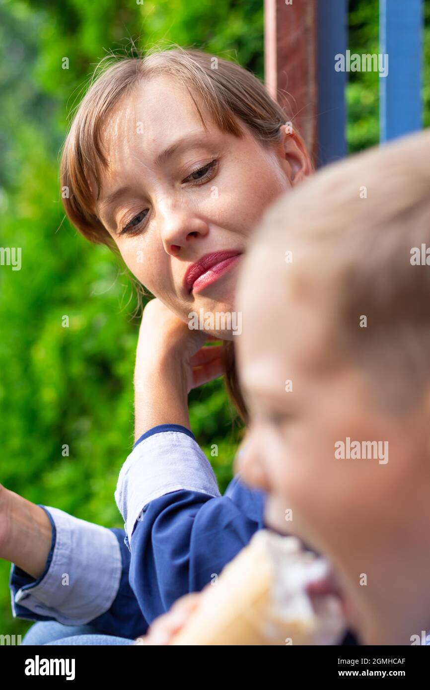 Preschooler ragazzo con mamma che mangia gelato sul portico di una casa nel villaggio in una giornata estiva di sole. Messa a fuoco selettiva. Verticale Foto Stock