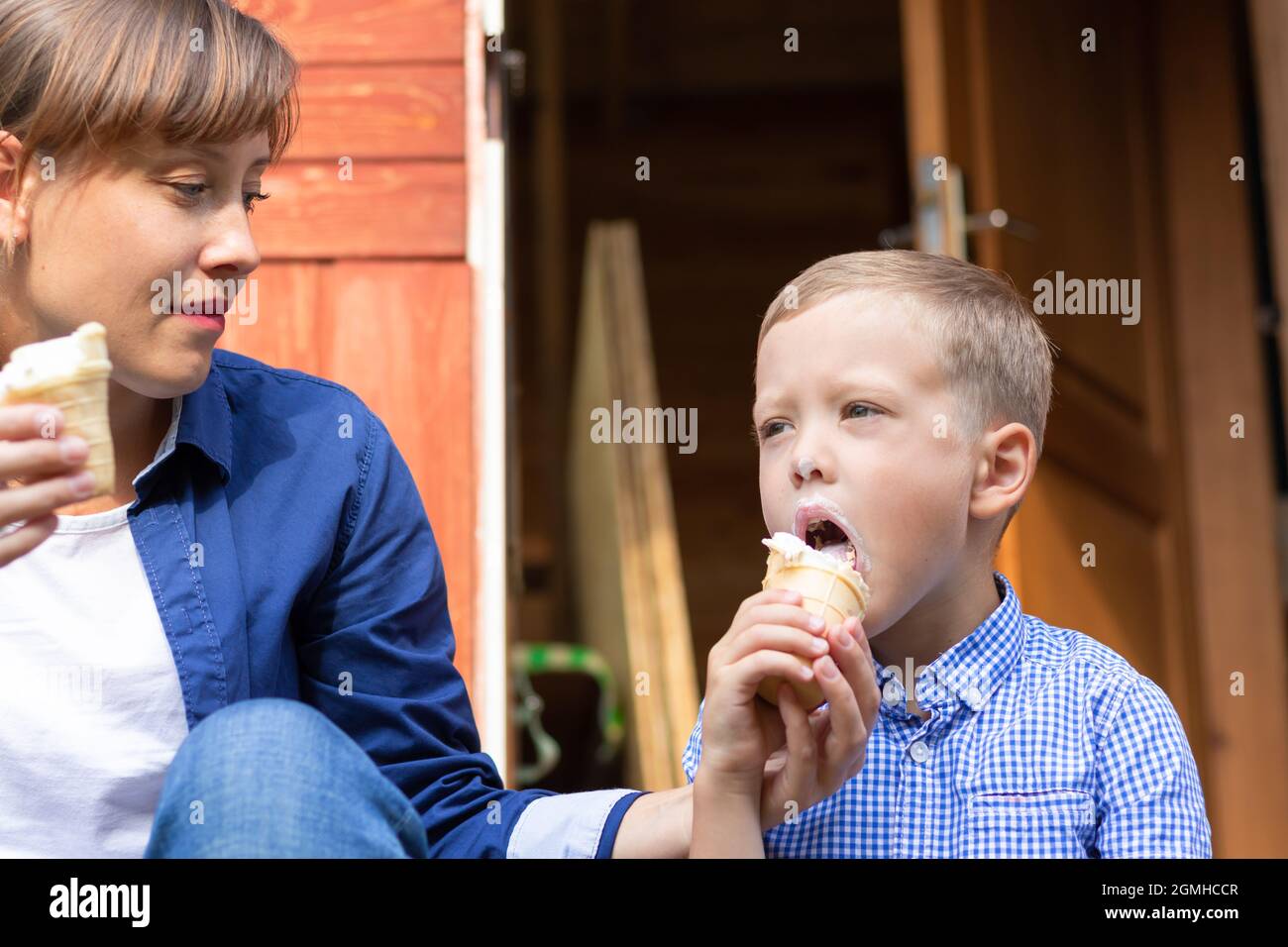 Preschooler ragazzo con mamma che mangia gelato sul portico di una casa nel villaggio in una giornata estiva di sole. Messa a fuoco selettiva. Verticale Foto Stock