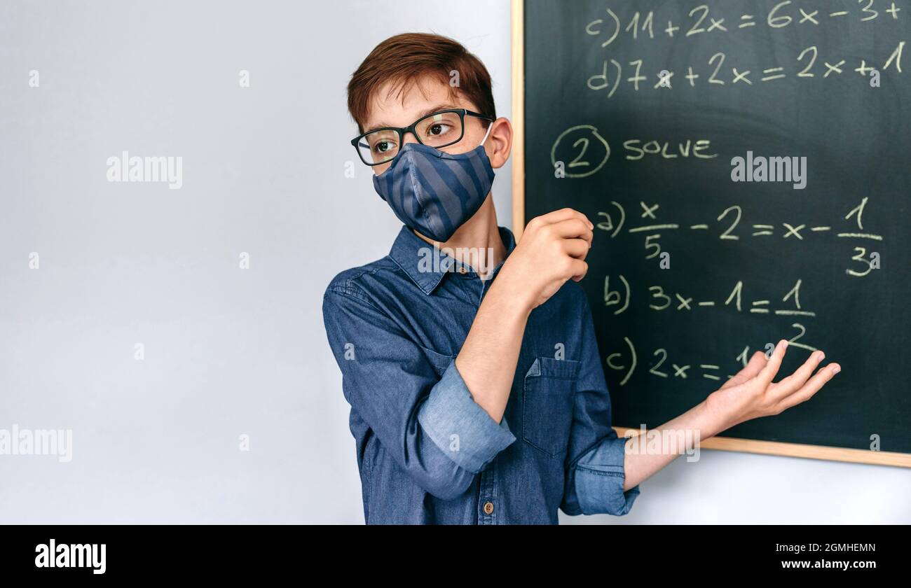 Ragazzo con maschera risolvere esercizi di matematica su lavagna Foto Stock
