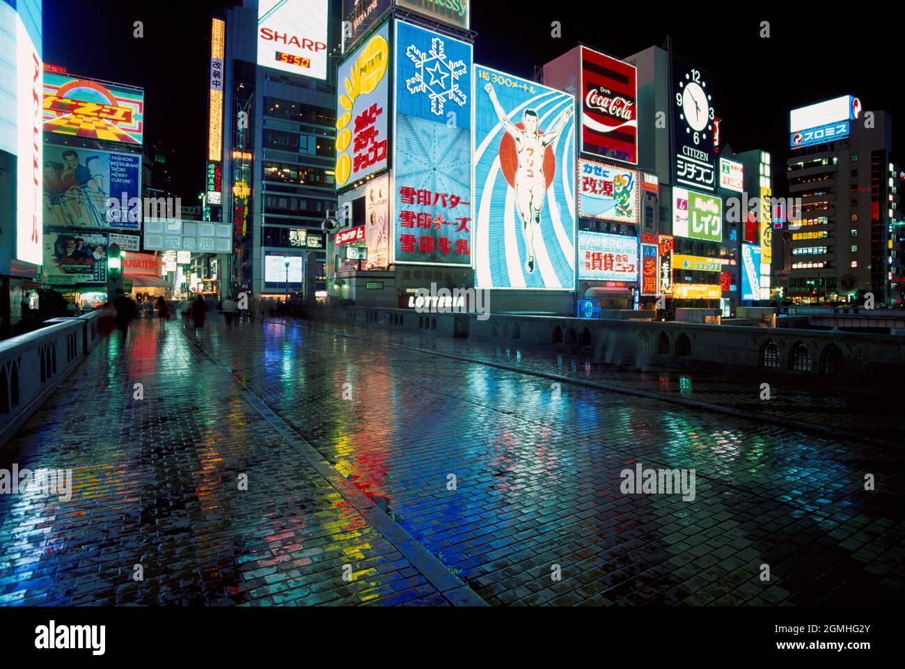 Giappone. La città di Osaka di notte. Segnali pubblicitari al neon riflessi su pavimentazione bagnata. Foto Stock