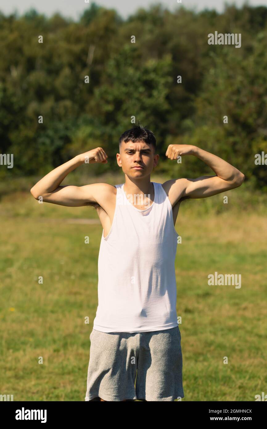 Un ragazzino di 18 anni in cima senza maniche a fine estate, flettendo i muscoli delle braccia Foto Stock