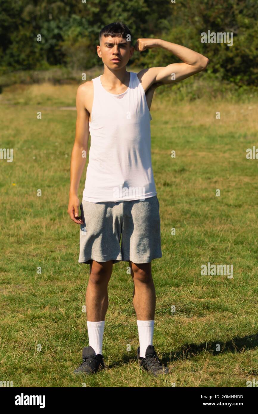Un ragazzino di 18 anni in cima senza maniche a fine estate, flettendo i muscoli delle braccia Foto Stock