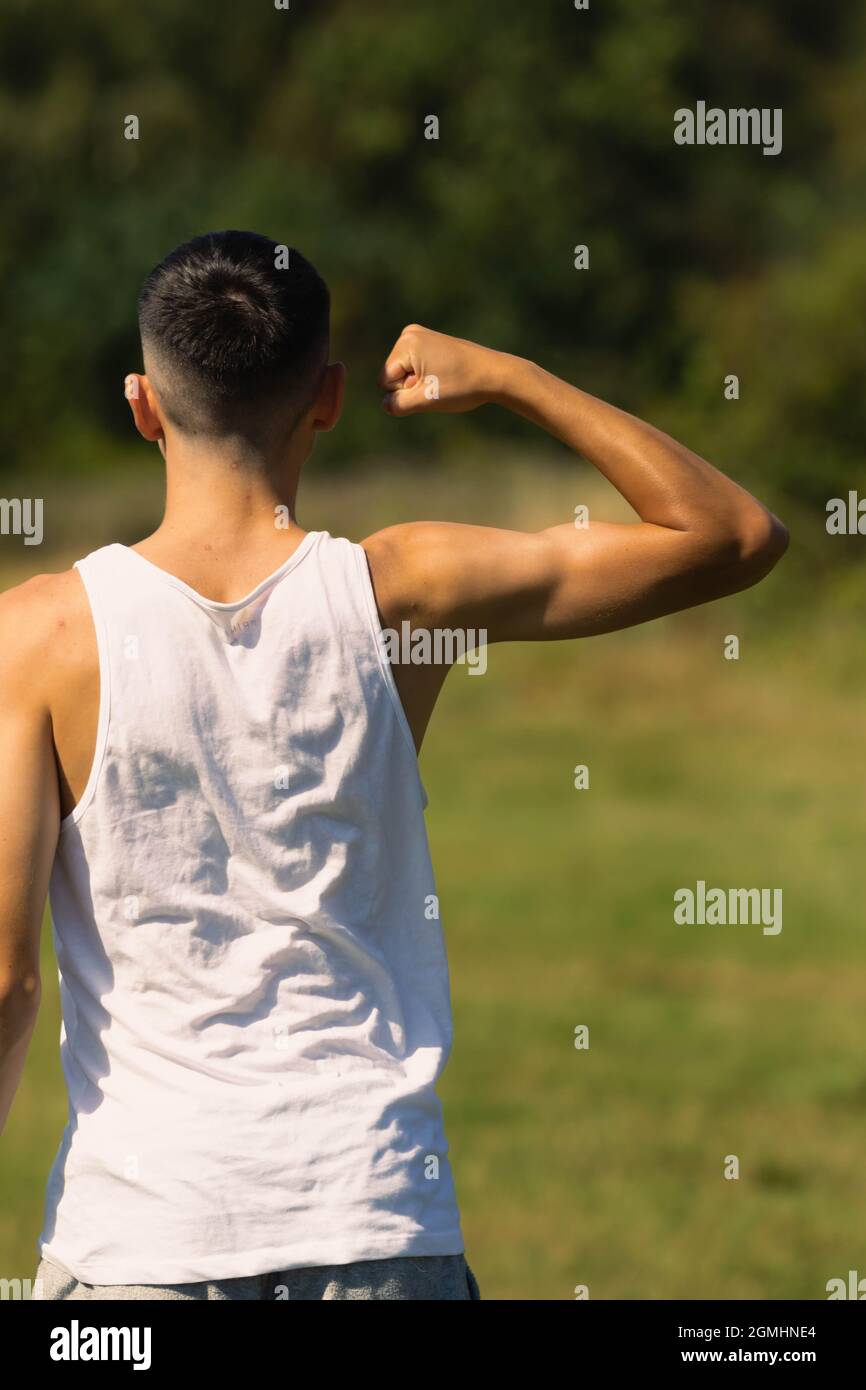 Un ragazzino di 18 anni in cima senza maniche a fine estate, flettendo i muscoli delle braccia Foto Stock