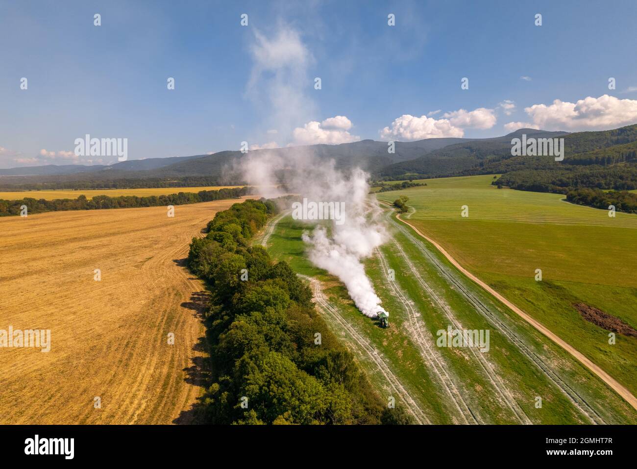 Vista aerea di un trattore che diffonde calce su campi agricoli per migliorare la qualità del suolo dopo la mietitura autunnale. L'uso di polvere di calce per neutralizzare Foto Stock