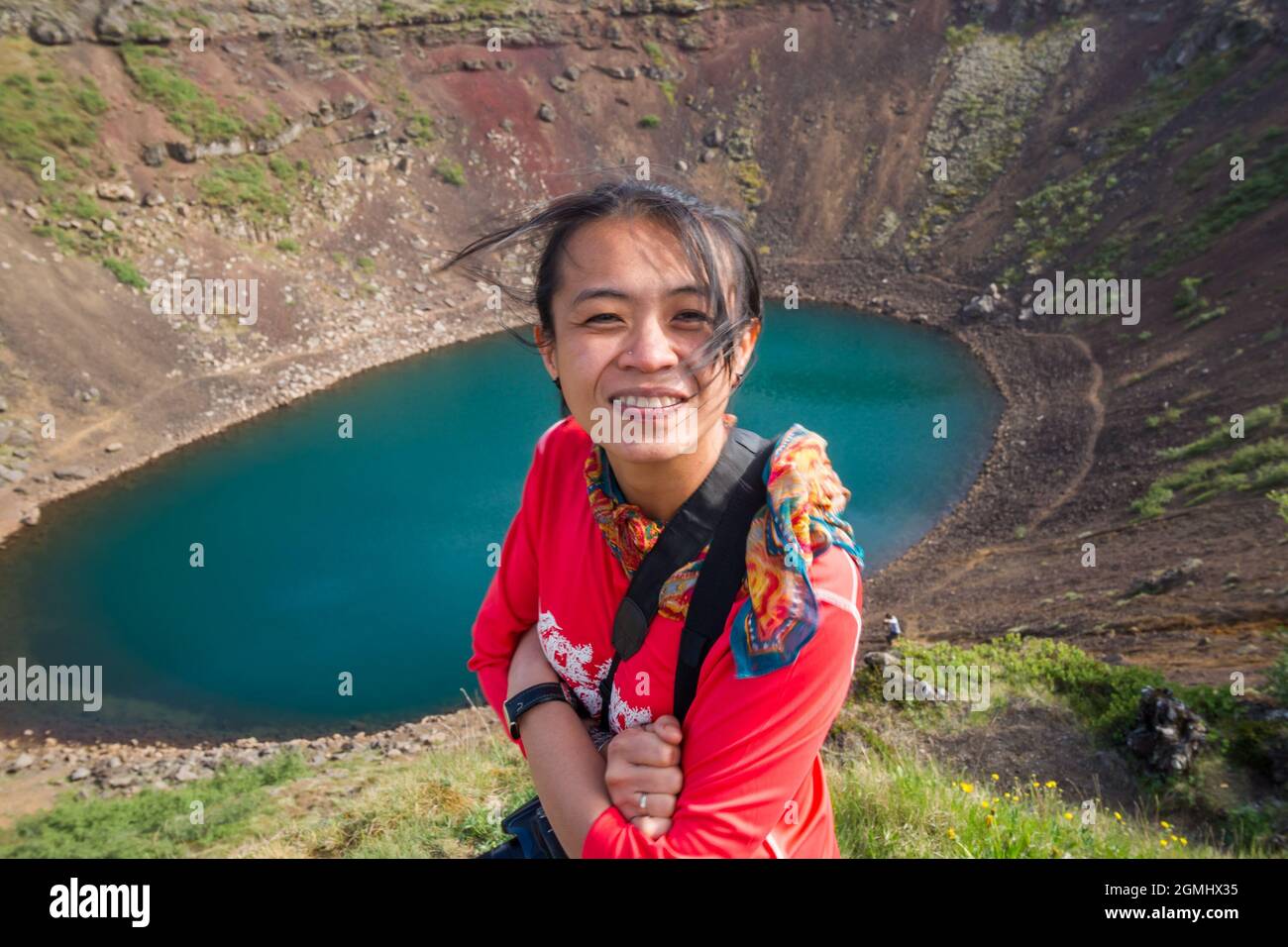 Asian lady in maglietta rossa nella parte anteriore di un color turchese del lago del cratere in Islanda Foto Stock