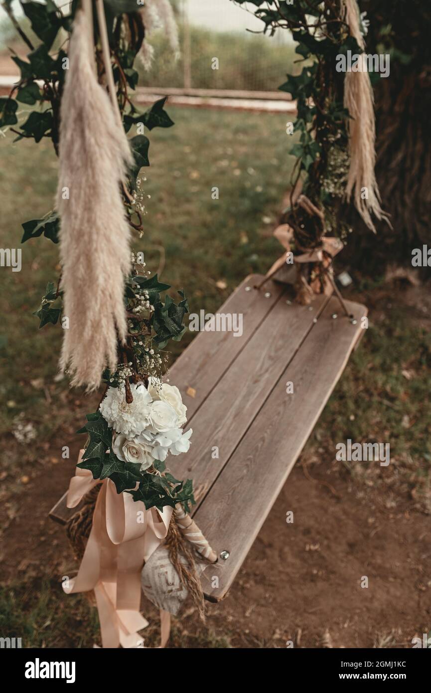 Un'altalena di legno decorata con fiori è appesa su un albero nel cortile.  Decorazioni per matrimoni Foto stock - Alamy