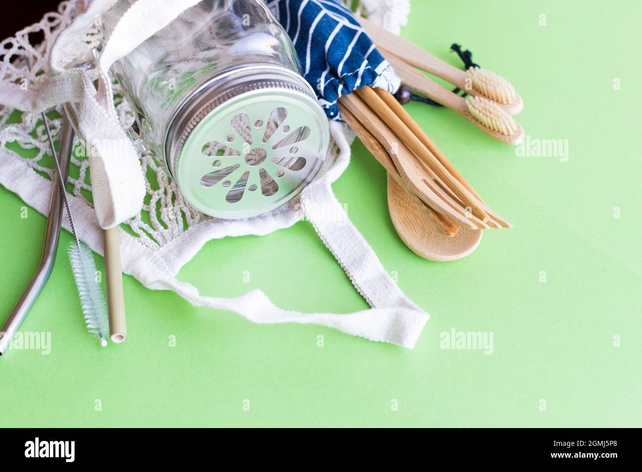 Concetto di zero sprechi. Sacchetto di cotone, posate di bambù e spazzolino da denti, vaso di vetro mason, cannucce di metallo e bambù su sfondo verde. Vita sostenibile. Eco f Foto Stock