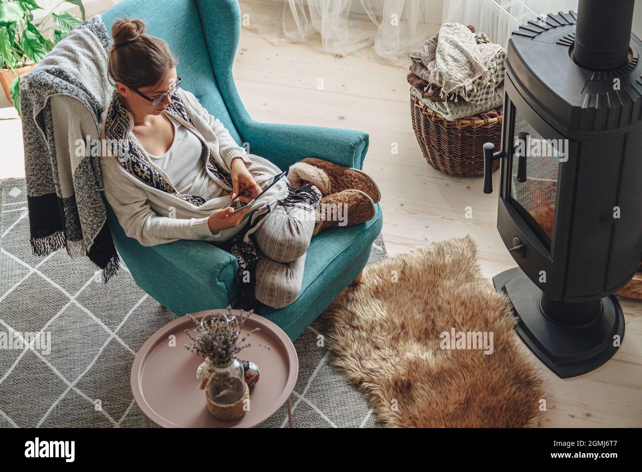 donna accanto al camino, seduta in una comoda poltrona, con un caldo Foto Stock