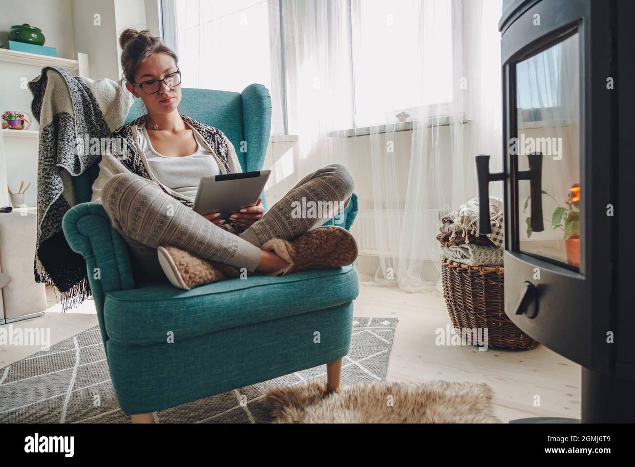 donna accanto al camino, seduta in una comoda poltrona, con un caldo Foto Stock