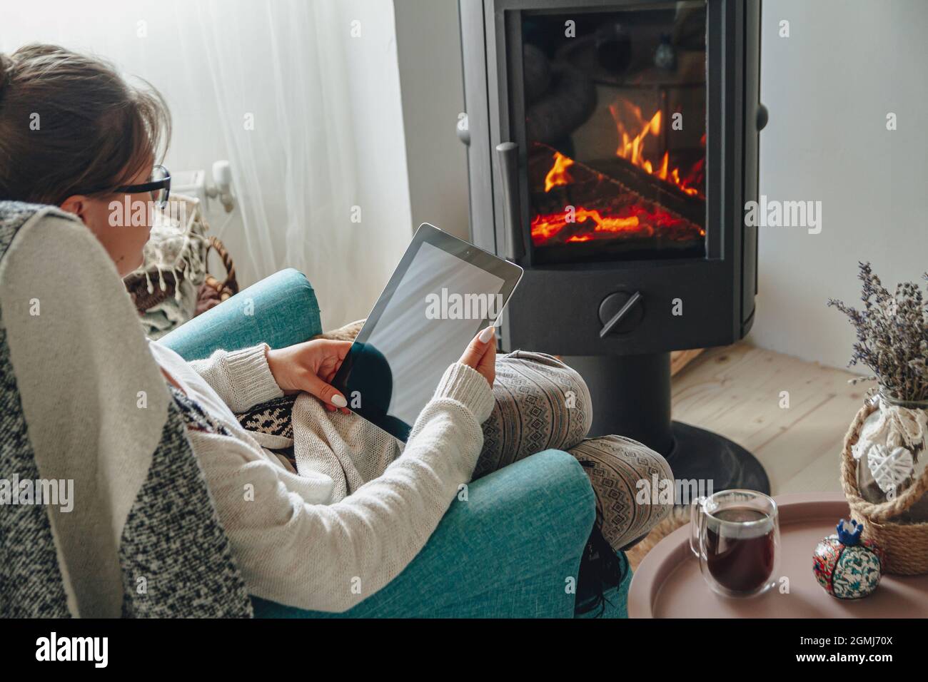 donna accanto al camino, seduta in una comoda poltrona, con un caldo Foto Stock