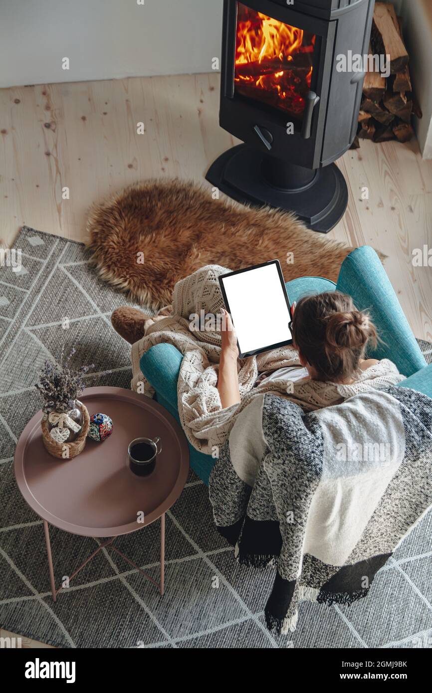 donna accanto al camino, seduta in una comoda poltrona, con un caldo Foto Stock
