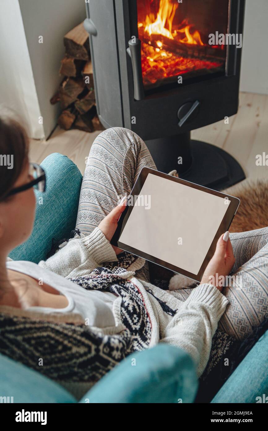 donna accanto al camino, seduta in una comoda poltrona, con un caldo Foto Stock