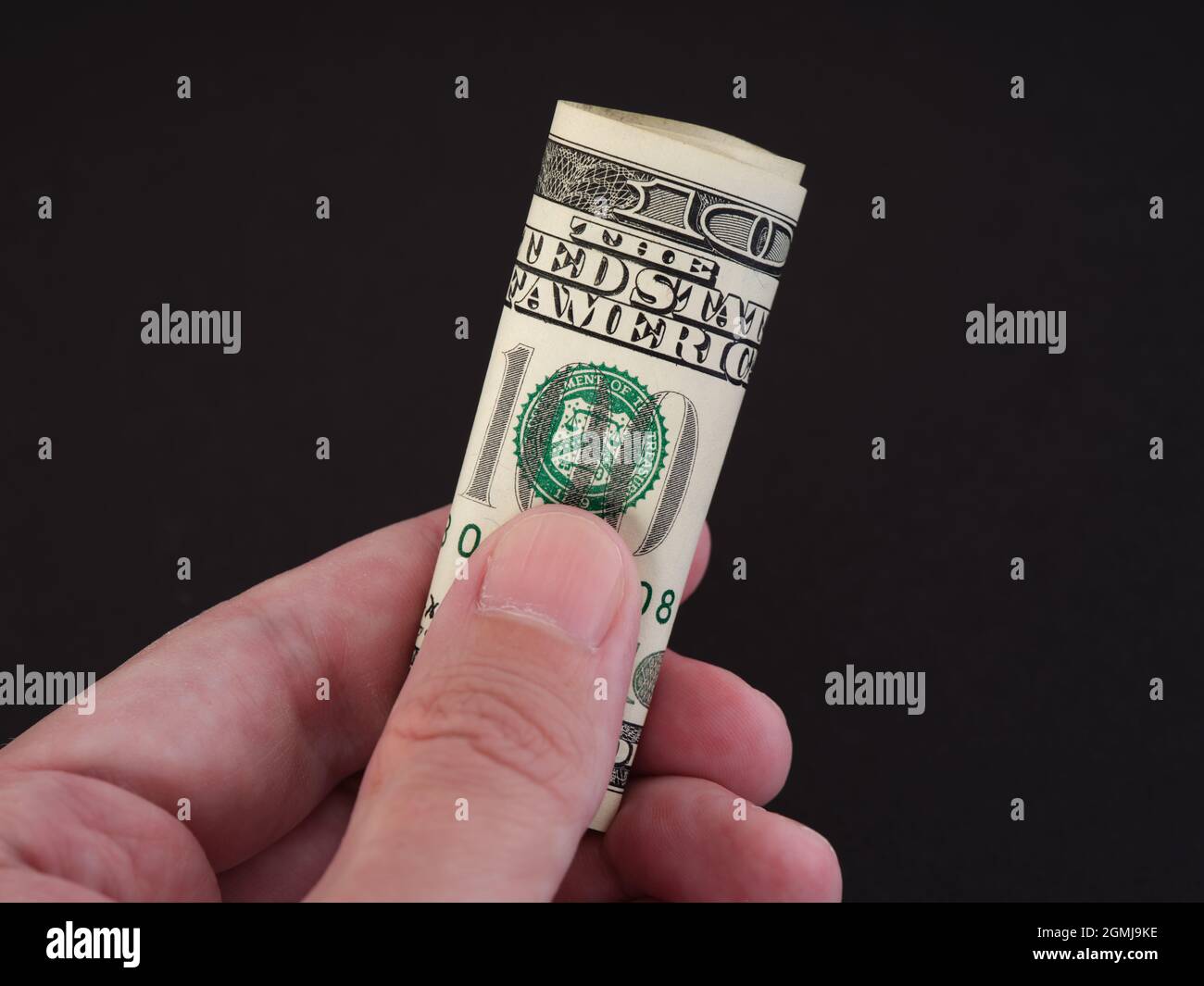 Un uomo che tiene in mano un conto di cento dollari piegato. Tasto basso. Primo piano. Foto Stock