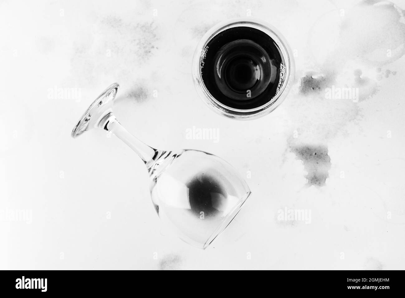 un bicchiere di vino rosso e un bicchiere rovesciato con i resti di vino su uno sfondo bianco adrenato e macchiato con vista dall'alto del vino, foto bianco nero Foto Stock