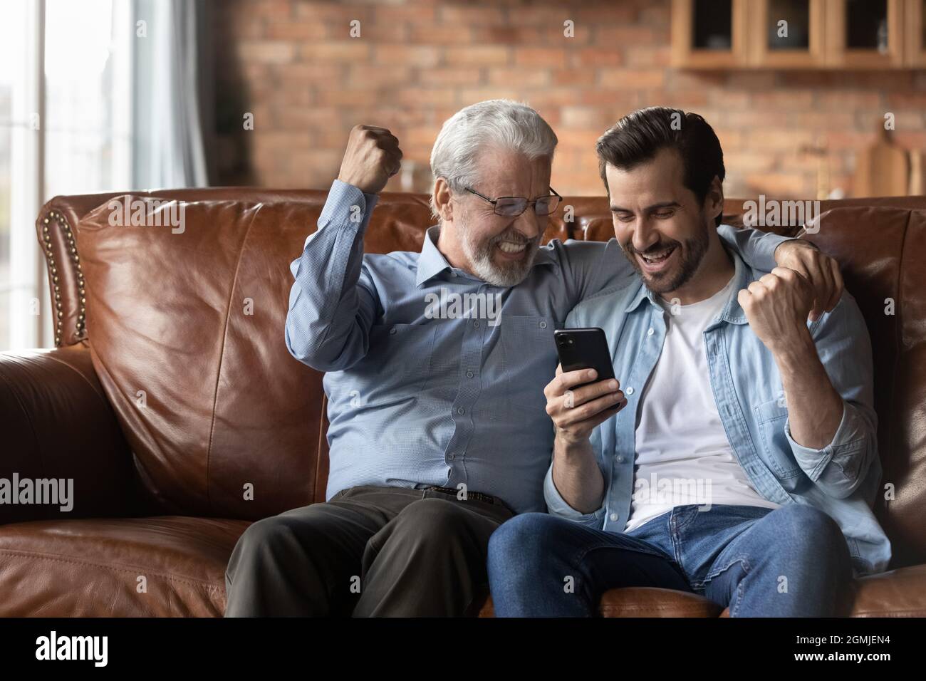 Due generazioni di uomini entusiasti di celebrare il successo utilizzando lo smartphone Foto Stock