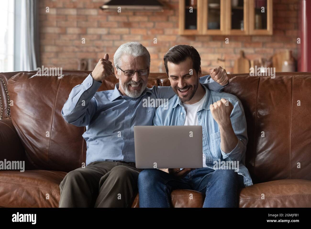 Il padre e il figlio maturi che festeggiavano il successo, usando il laptop Foto Stock