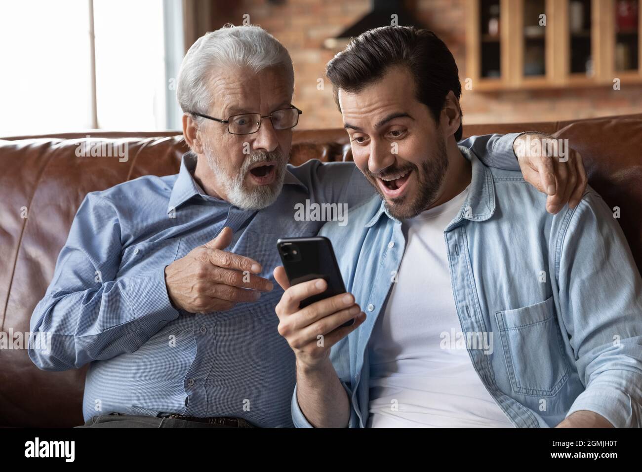 Overjoyed sorprende due generazioni di uomini che guardavano lo schermo del telefono Foto Stock