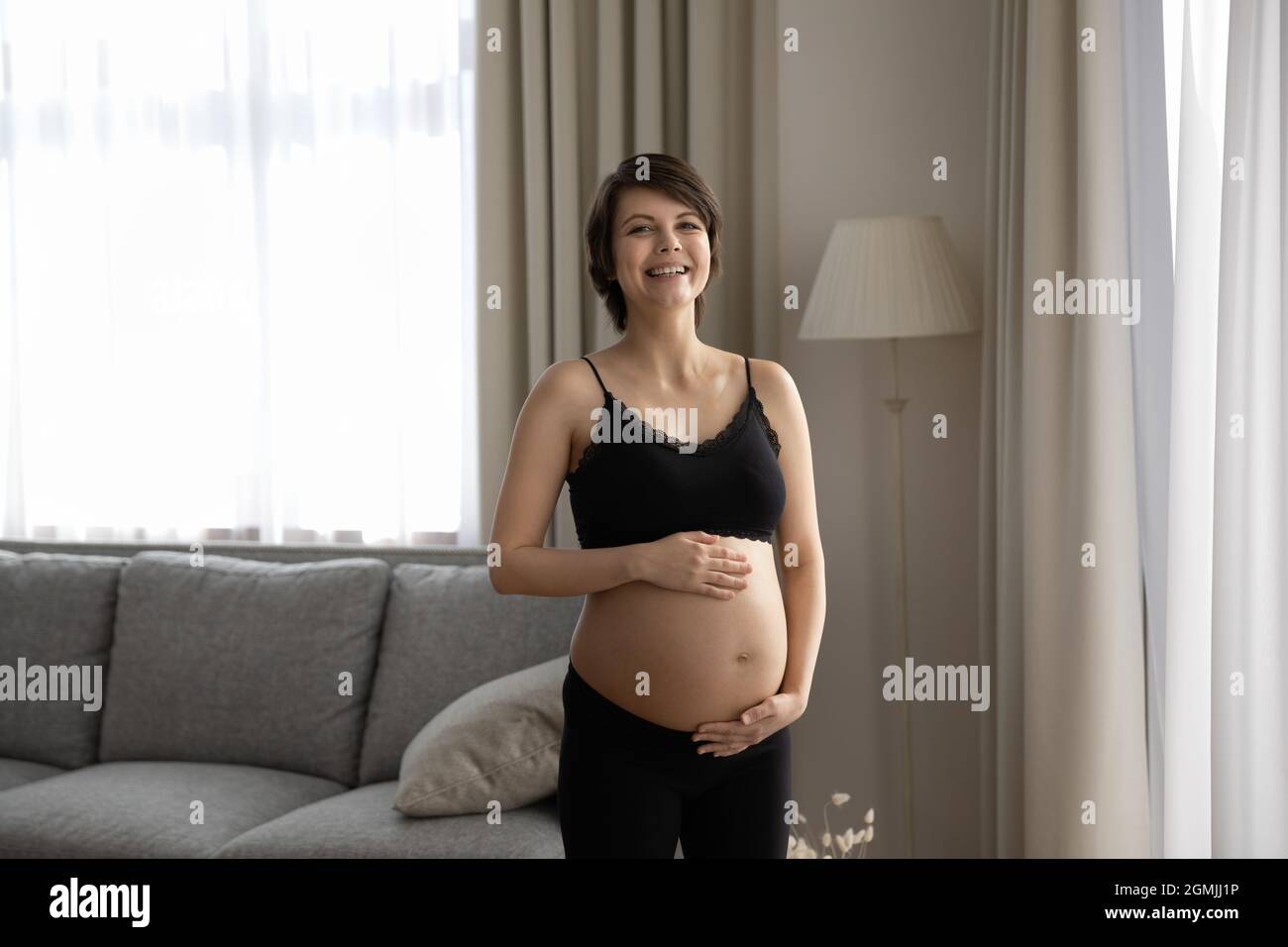 Ritratto di giovane donna incinta che ride tenendo le mani sul ventre Foto Stock