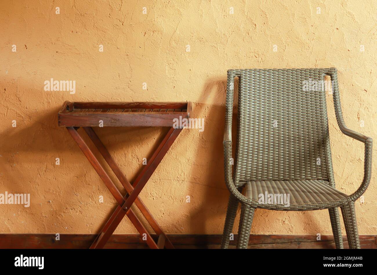 Sedie in tessuto e un tavolo in legno poggiano su un robusto muro in cemento dipinto di giallo. Foto Stock