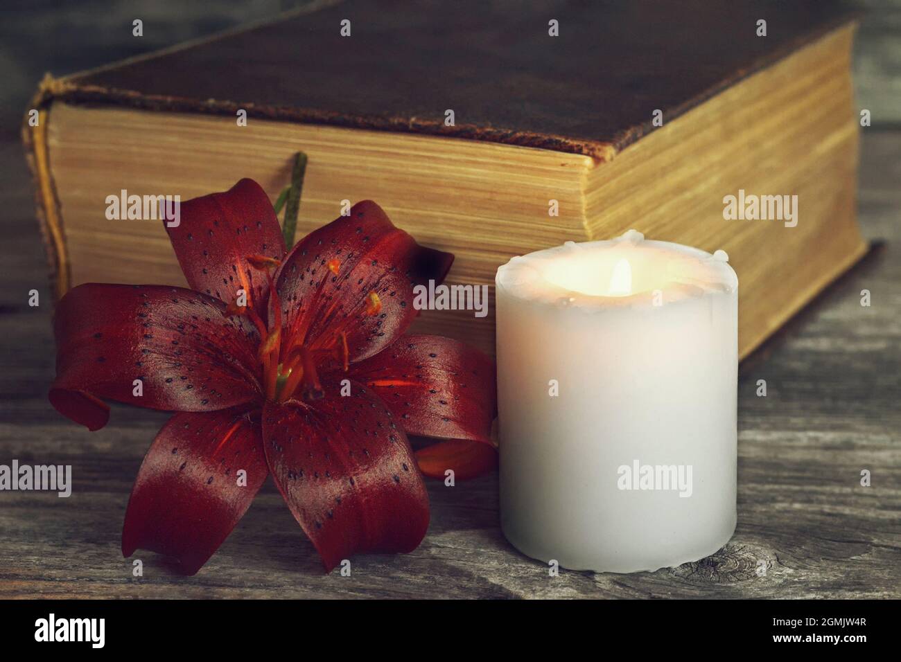 Candela bianca, fiore di giglio scuro e libro chiuso. Scheda di condoglianze Foto Stock