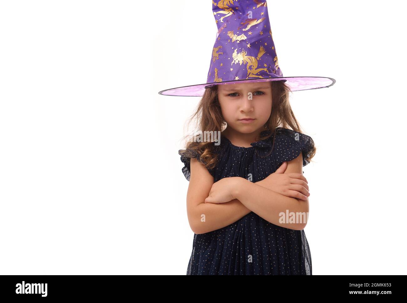 Ritratto di bella piccola strega ragazza arrabbiata con un cappello mago e vestito in elegante abito carnevale, guardando la macchina fotografica in posa con braccio incrociato Foto Stock