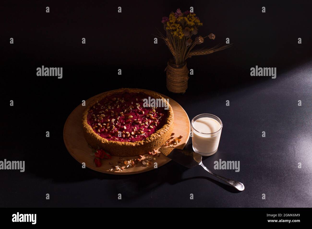 Cheesecake di frutta dolce con bicchiere di latte e bouquet secco su sfondo nero. Foto Stock