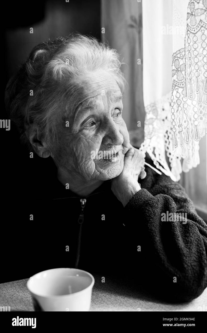 Ritratto di una vecchia signora nella sua casa vicino alla finestra. Foto in bianco e nero. Foto Stock