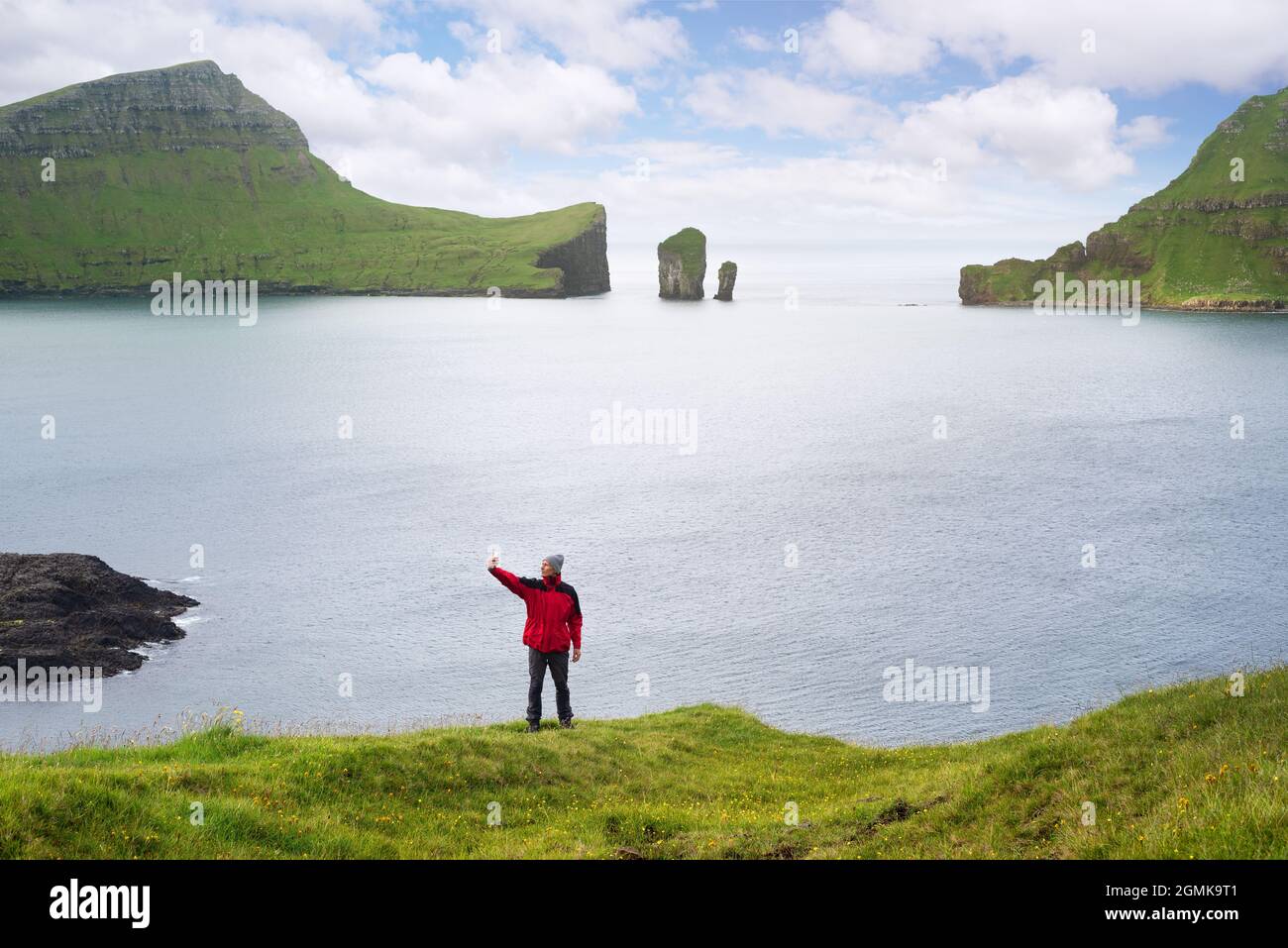 Il viaggiatore prende un selfie sullo sfondo delle pile di mare di Drangarnir e l'isolotto di Tindholmur sulle Isole Faroe Foto Stock