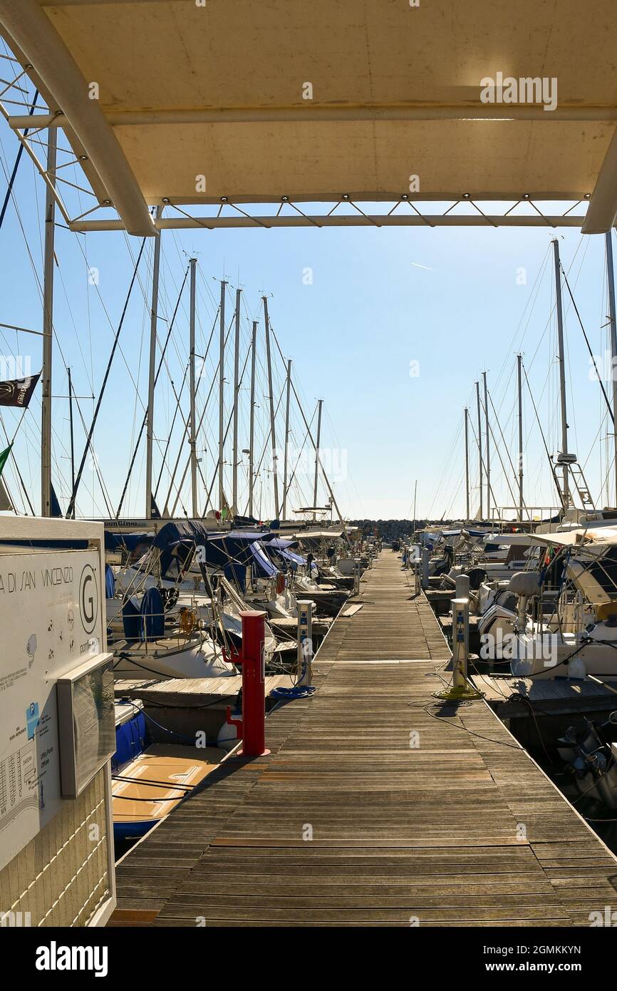 Una vista lungo una passerella galleggiante in legno al porto di San Vincenzo con yacht privati ormeggiati su entrambi i lati, Livorno, Toscana, Italia Foto Stock