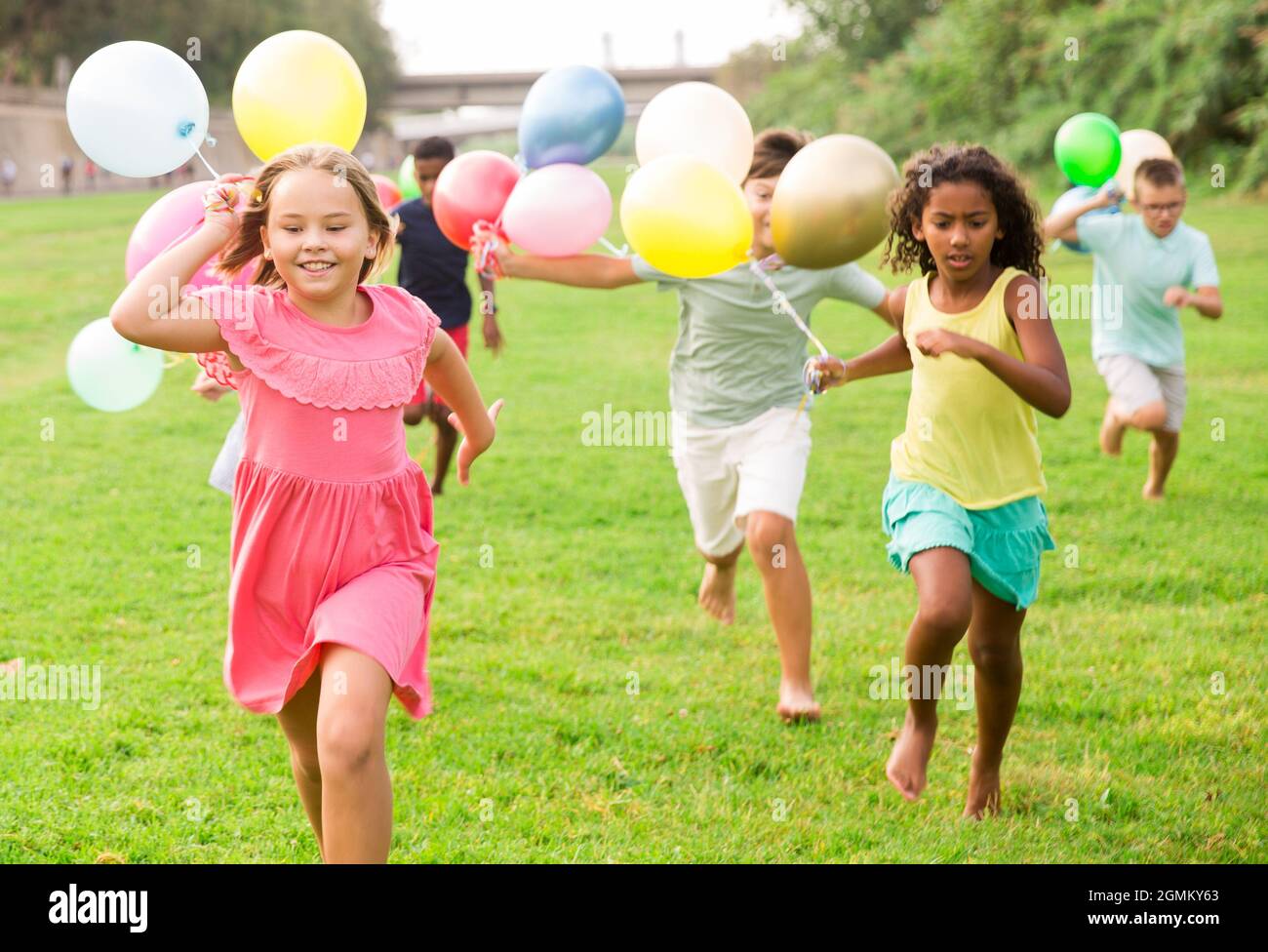 Ragazzi e ragazze con palloncini che corrono thruogh Field Foto Stock