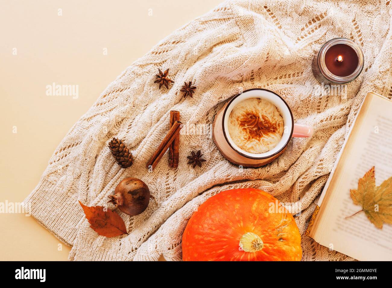 Una tazza di latte di zucca sul tavolo con libro, candela, foglie gialle e spezie su un fondo maglione a maglia. Concetto autunnale, vista dall'alto, piatto Foto Stock