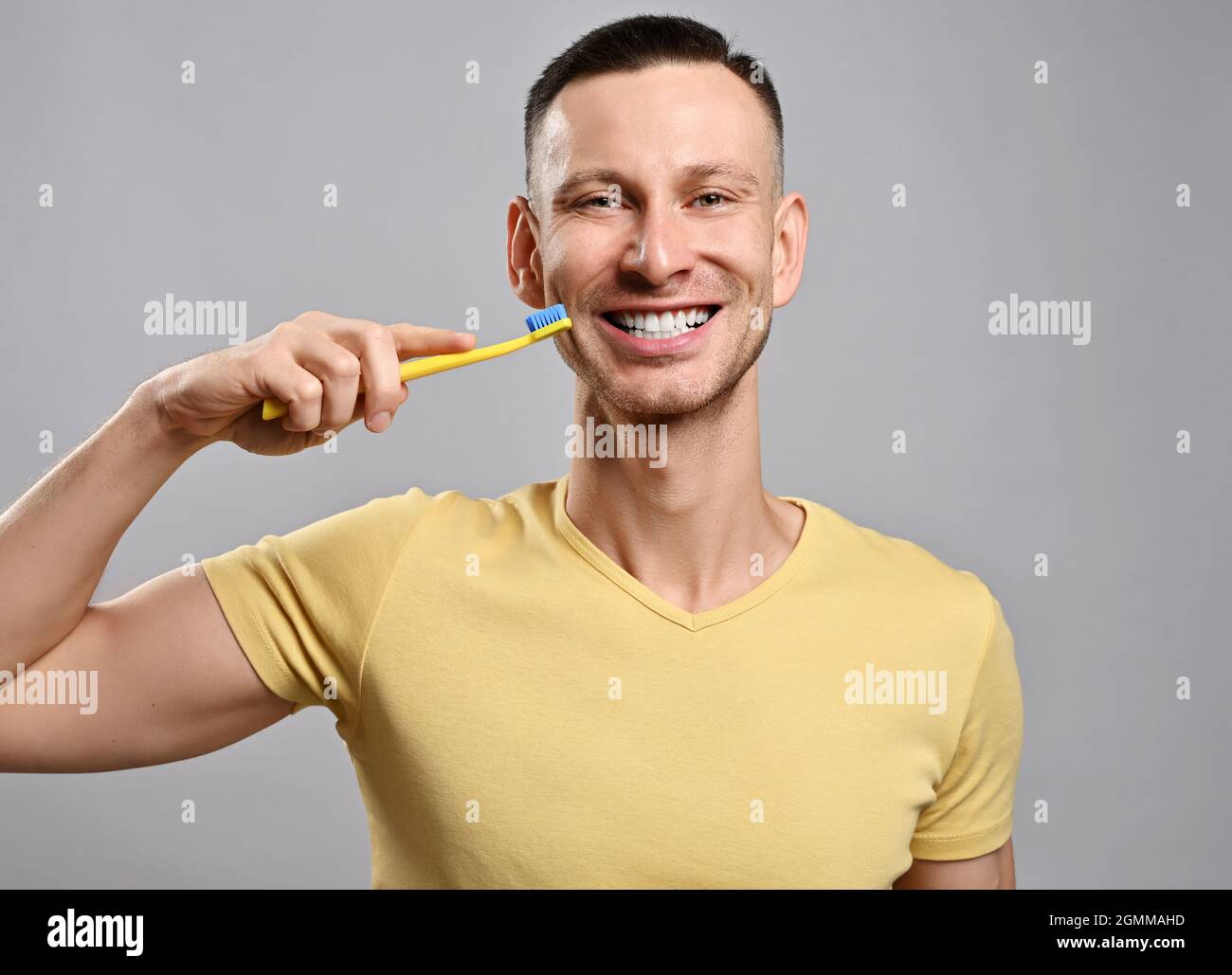 Ritratto di uomo adulto sorridente felice amichevole in t-shirt gialla con spazzolino dimostra i suoi sani denti bianchi Foto Stock